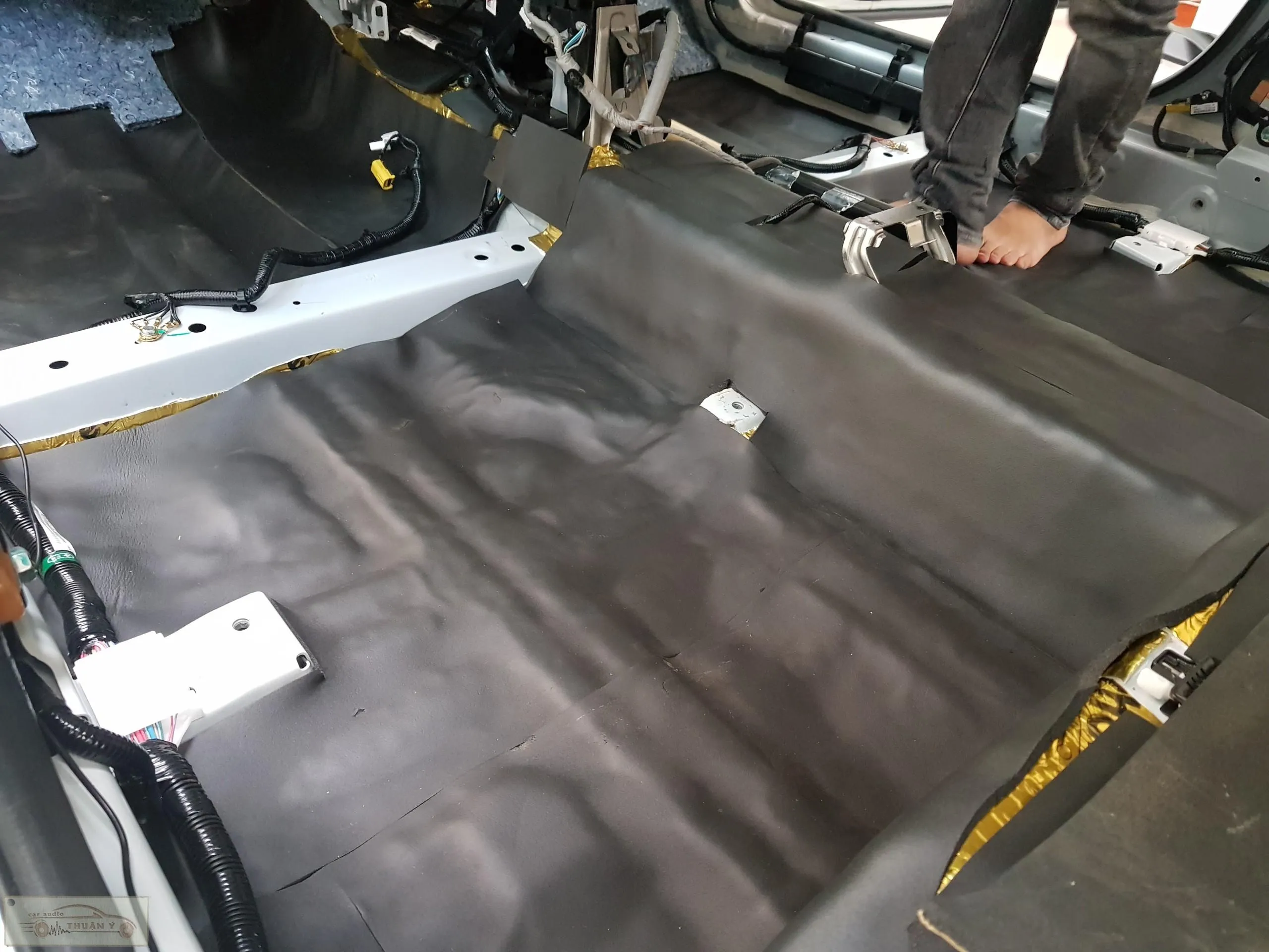 Kỹ thuật viên sử dụng dụng cụ chuyên dụng để miết và cố định vật liệu chống ồn lên sàn xe ô tô, đảm bảo độ bám dính tuyệt đối