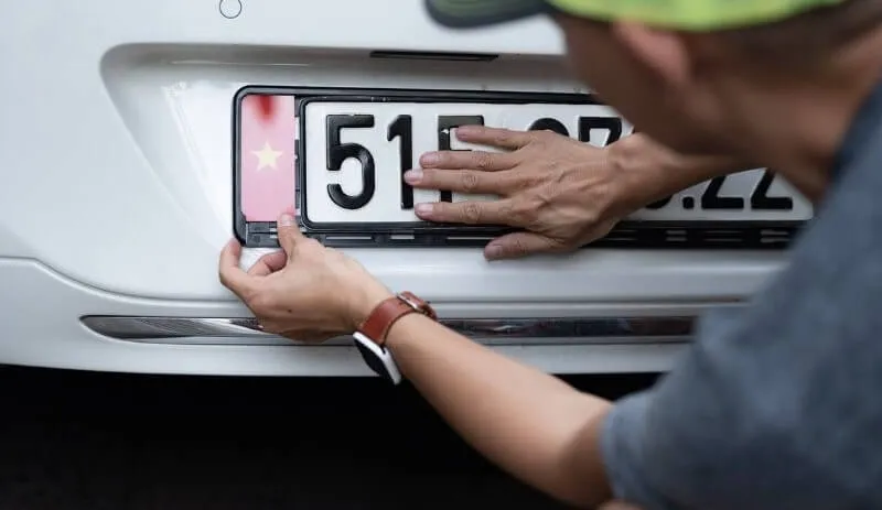 Người lái xe đang cẩn thận tháo chốt nhựa giữ biển số xe ô tô bằng dụng cụ chuyên dụng