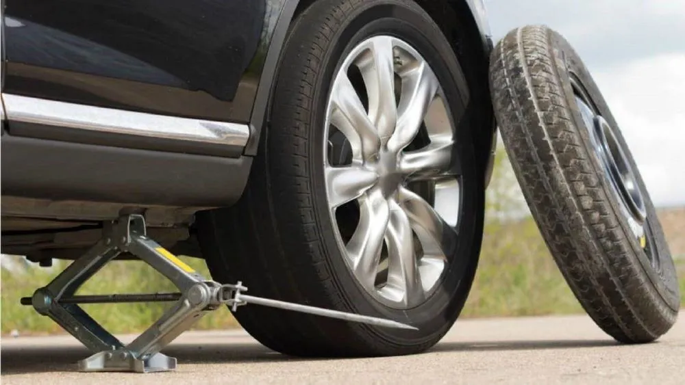 Tài xế đang đặt kích nâng xe ô tô tại vị trí gầm xe để tiến hành tự thay lốp xe