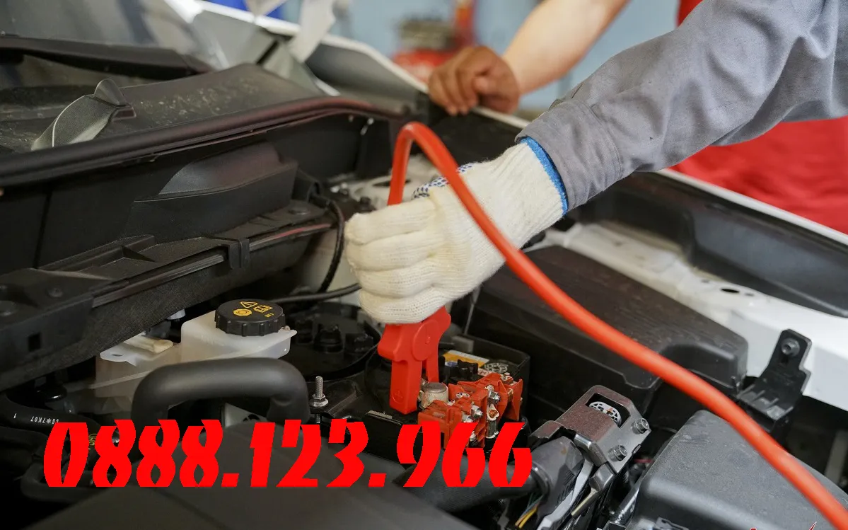 Kỹ thuật viên đang kích điện ắc quy ô tô bằng dây cáp nối bình
