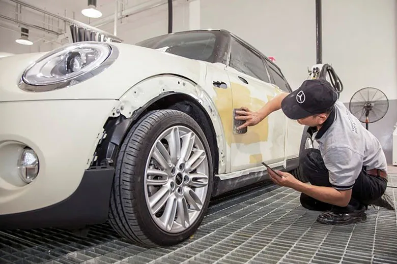 Kỹ thuật viên đang kiểm tra vết móp trên thân xe ô tô trước khi làm đồng sơn.