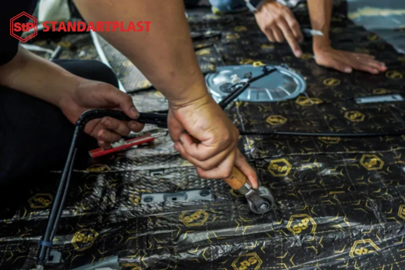 Thợ chuyên nghiệp đang lăn và ép chặt tấm cách âm ở vị trí sàn xe, đảm bảo hiệu quả chống rung và chống ù tối đa