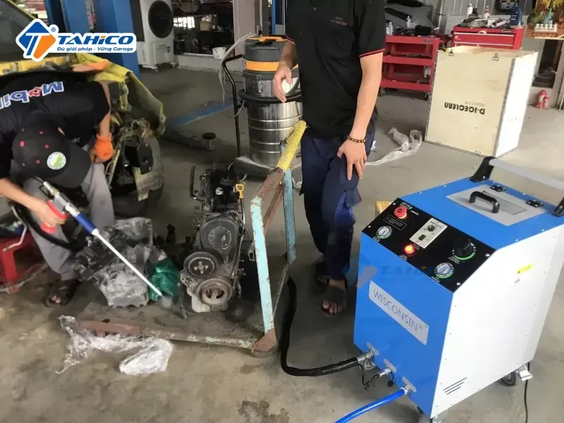 Kỹ thuật viên đang cầm súng phun đá khô của máy Wisconsin W9000 làm sạch bề mặt chi tiết xe