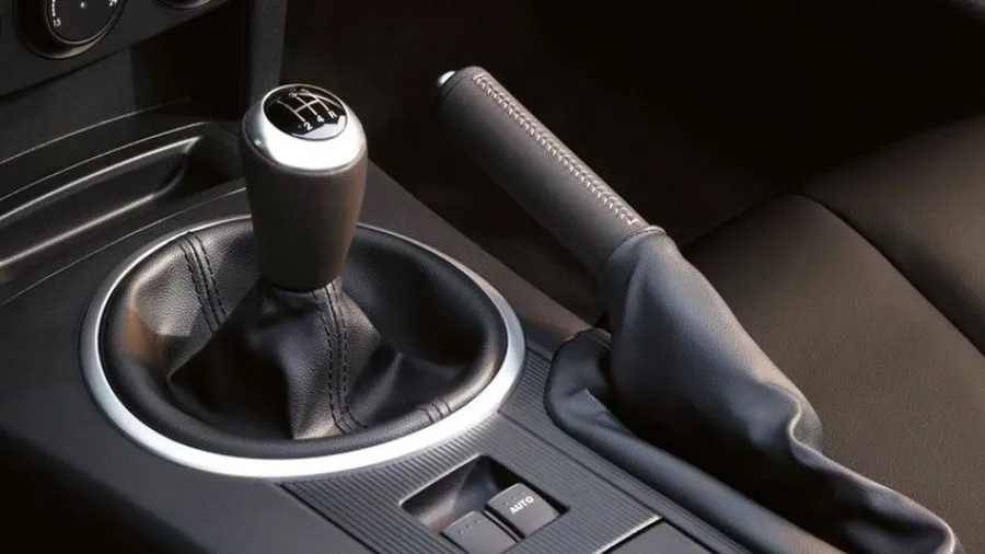 Một tài xế đang thực hiện thao tác kéo cần phanh tay cơ học nằm giữa hai ghế trước