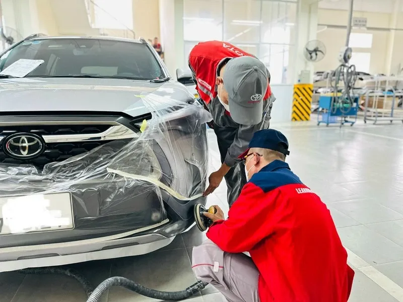 Kỹ thuật viên đang kiểm tra chất lượng sơn xe ô tô trong môi trường xưởng chuyên nghiệp